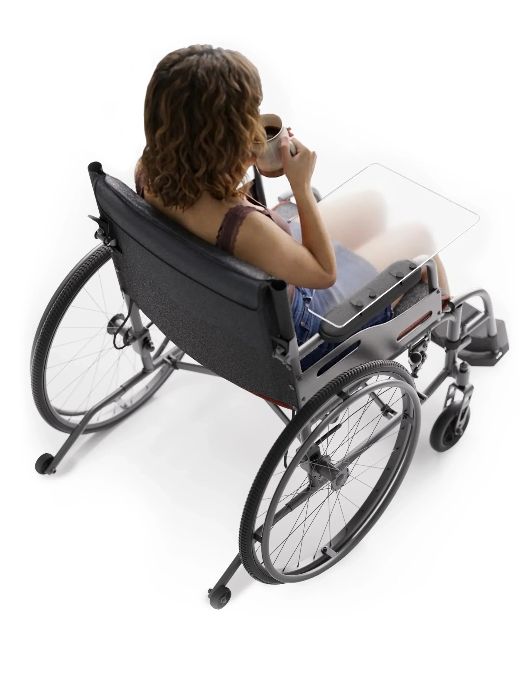 Person using a wheelchair with a transparent half tray accessory, holding a mug