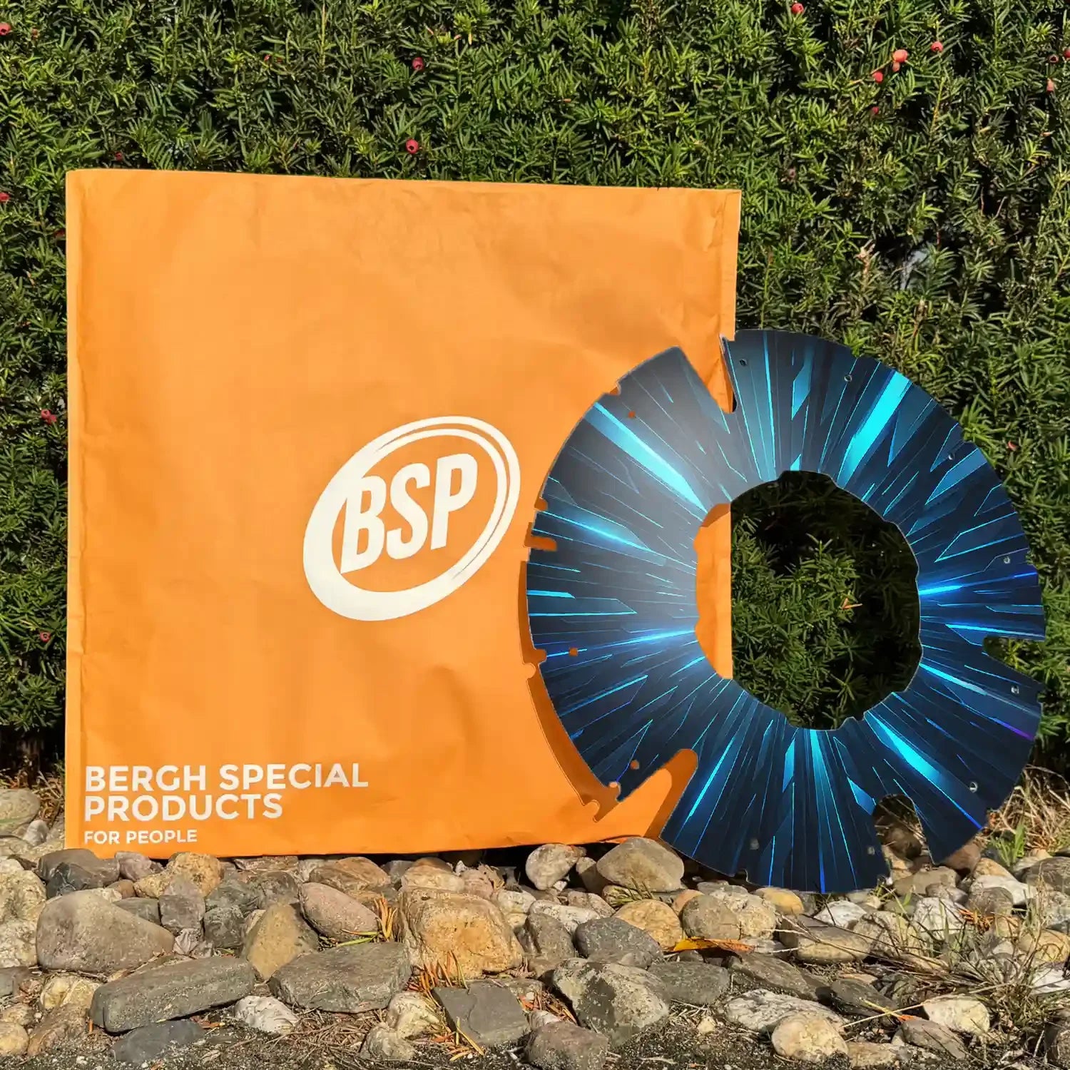 Printed wheelchair spoke guard with blue pattern on rocky ground near a green wall and orange bag