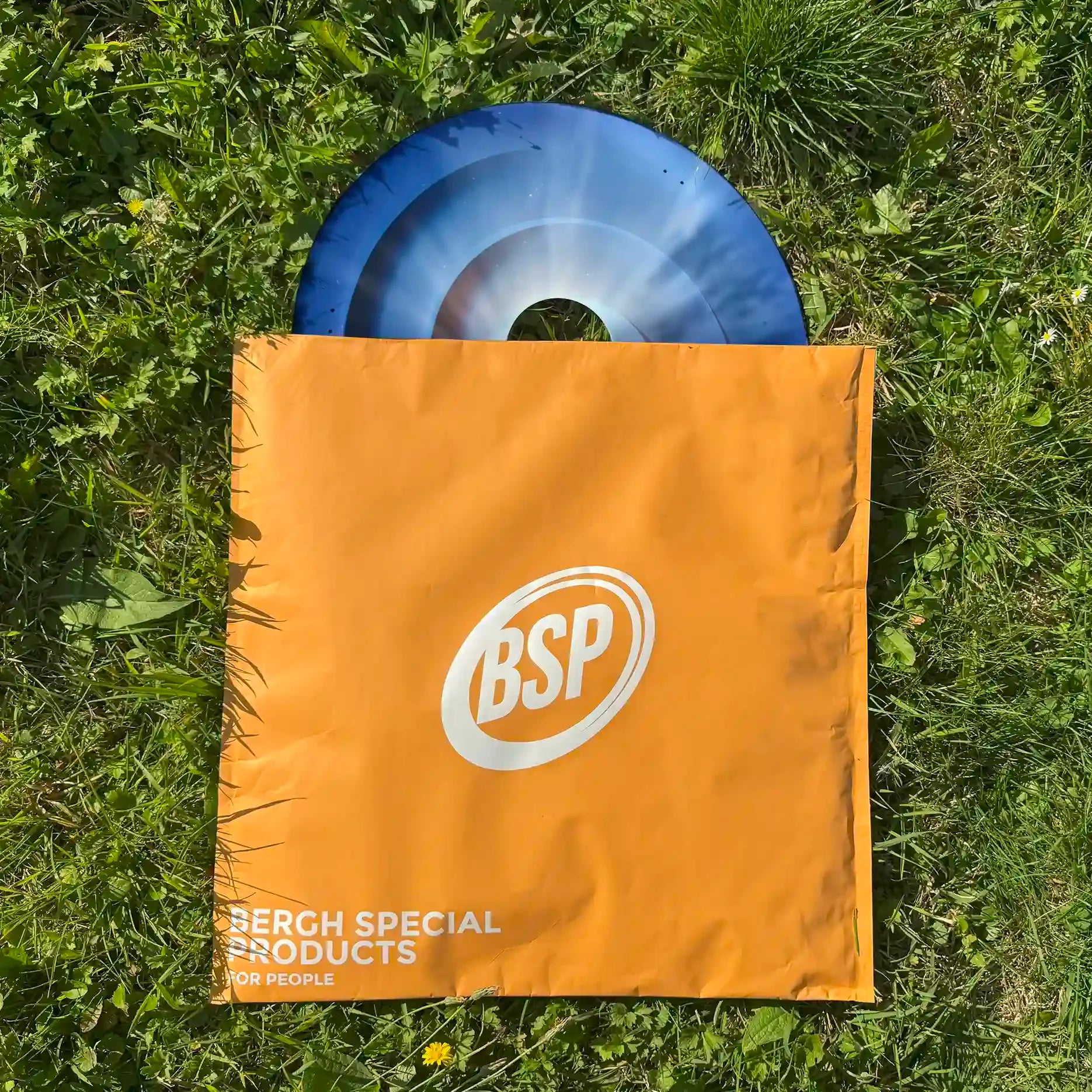 Blauer Wirbel-Rollstuhl-Speichenschutz teilweise in einer orangefarbenen BSP-Tasche auf grünem Gras
