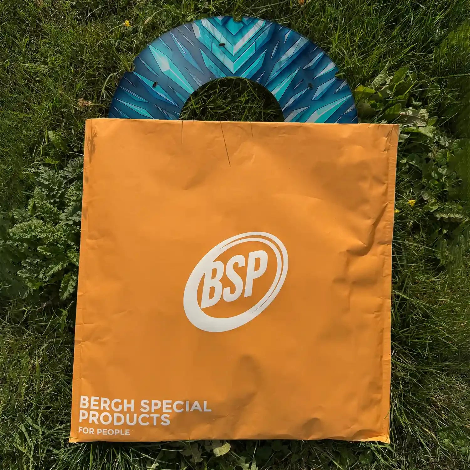 Printed wheelchair spoke guard with blue geometric design, partially covered by orange BSP bag on grass