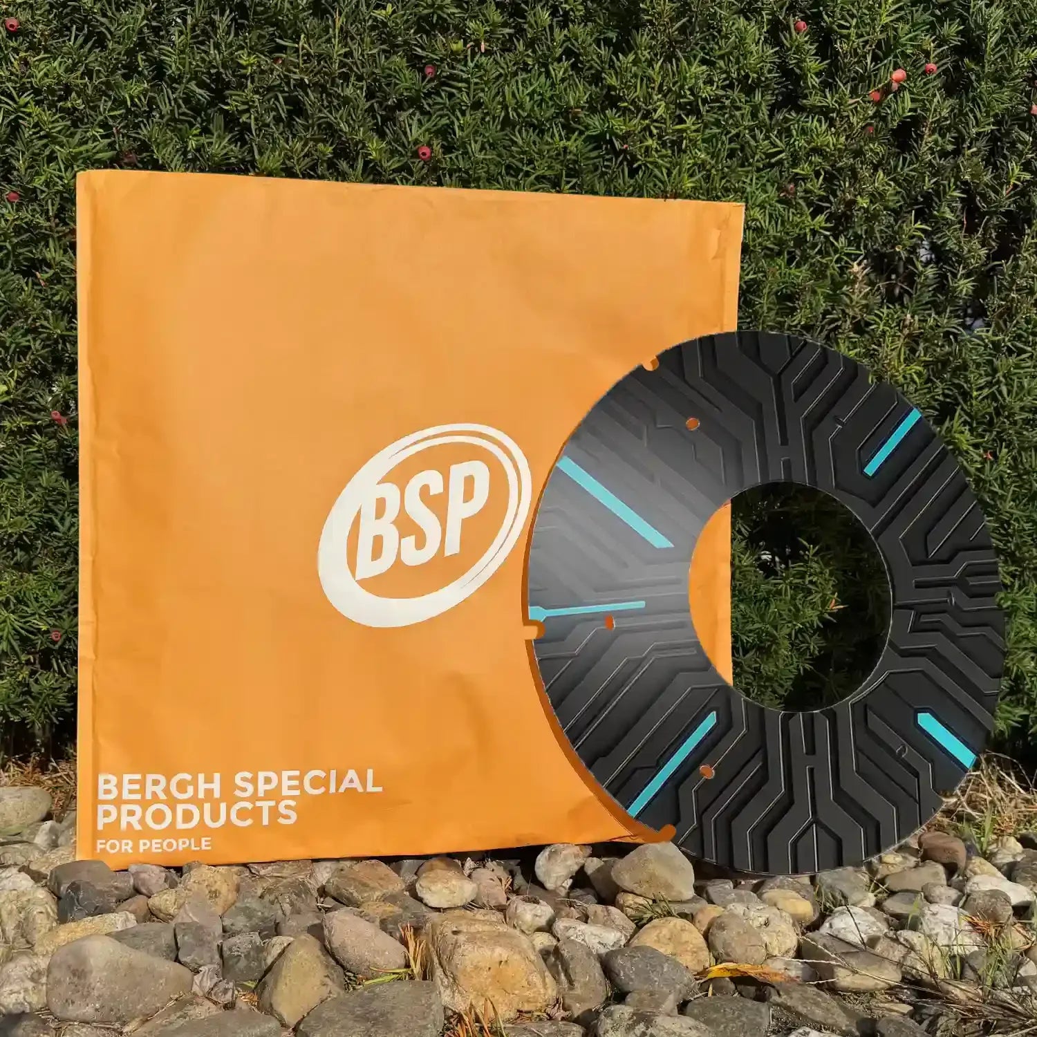 Moderner schwarz-blauer Rollstuhl-Speichenschutz auf Steinen nahe grüner Hecke, orangefarbene BSP-Tasche dahinter