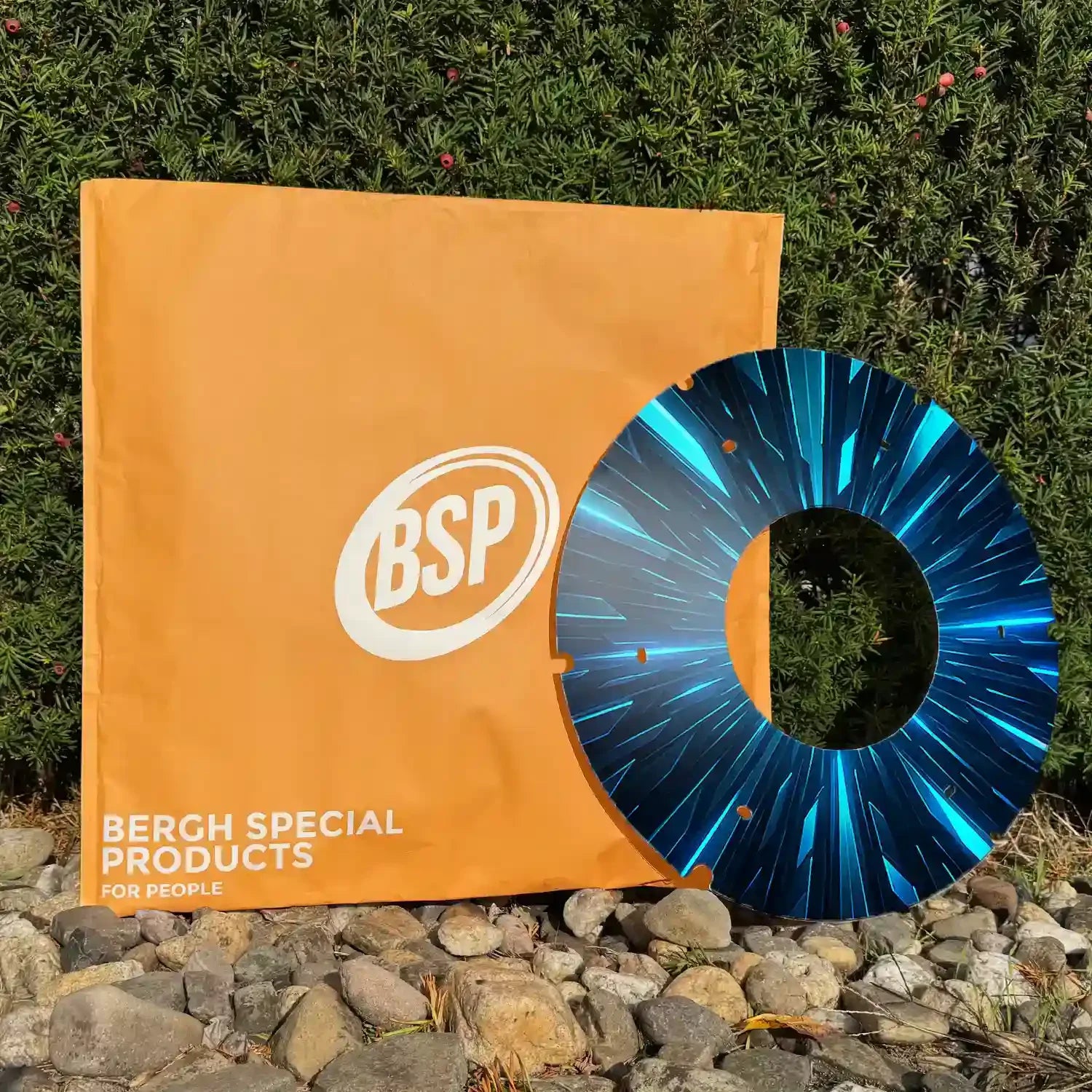Blue printed wheelchair spoke guard with radiant pattern, displayed outdoors on stones near a green bush.
