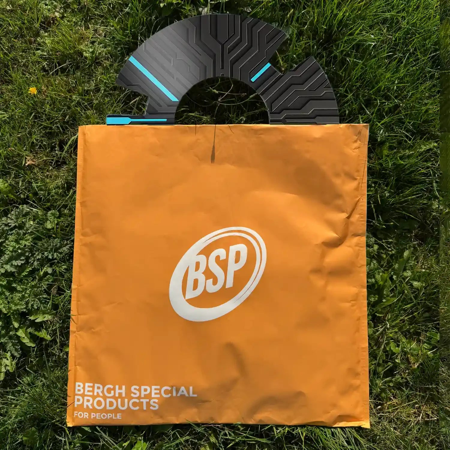 Bedruckter Rollstuhl-Speichenschutz mit Schaltkreisdesign neben orangefarbener BSP-Tasche auf Gras