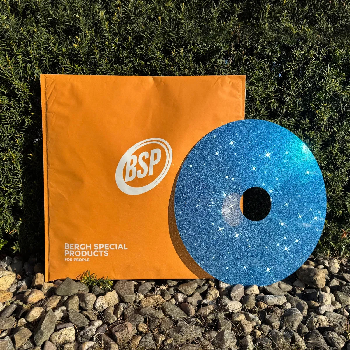 Blauer Glitzer-Rollstuhl-Speichenschutz mit Sternenmuster neben orangefarbener BSP-Verpackung auf Steinen