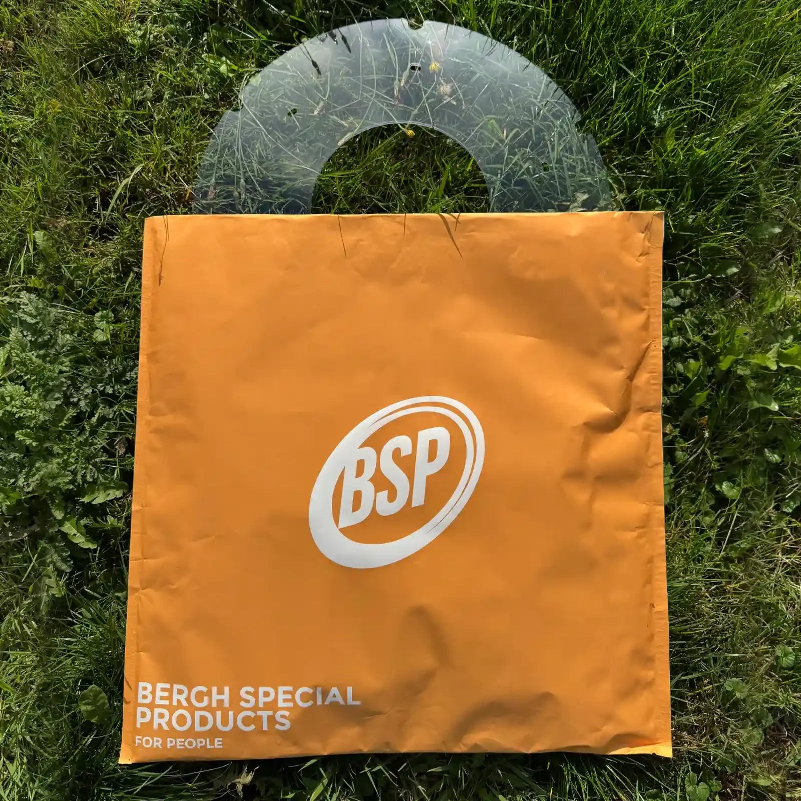 Transparent wheelchair spoke guard partially covered by orange BSP bag on green grass