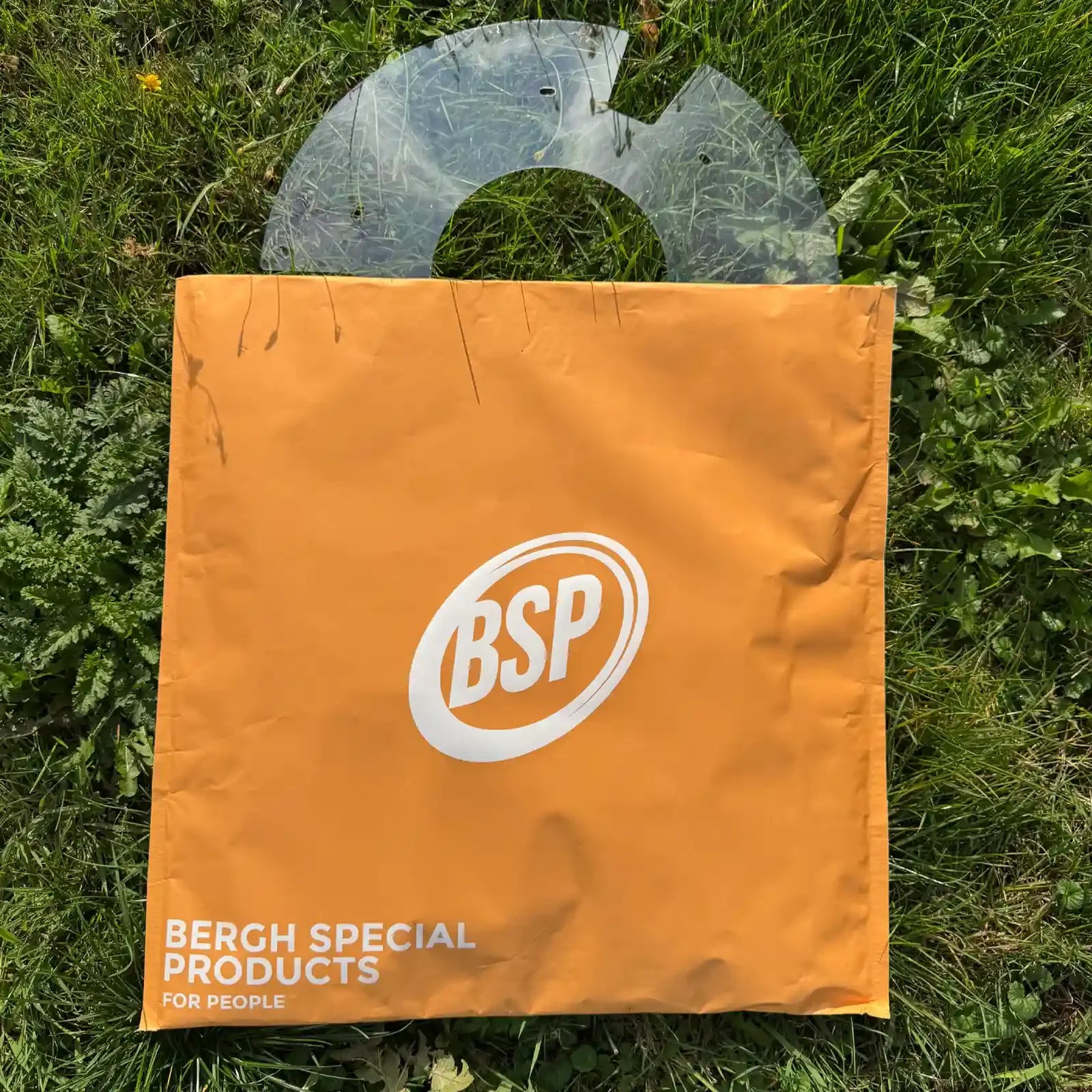 Transparenter Rollstuhl-Speichenschutz auf Gras mit orangefarbener BSP-Aufbewahrungstasche präsentiert