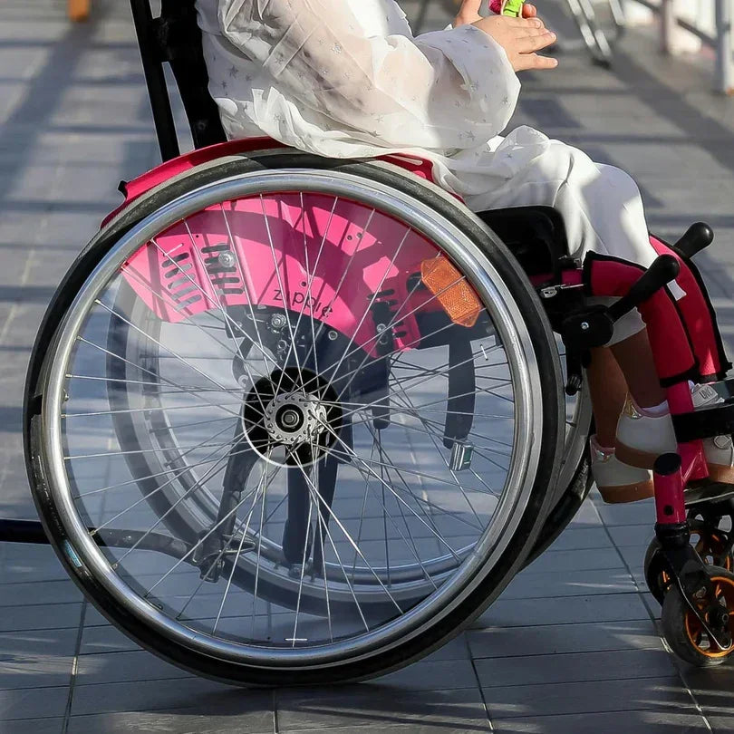 Girl in wheelchair with pink transparent spoke guards and wheelchair accessories