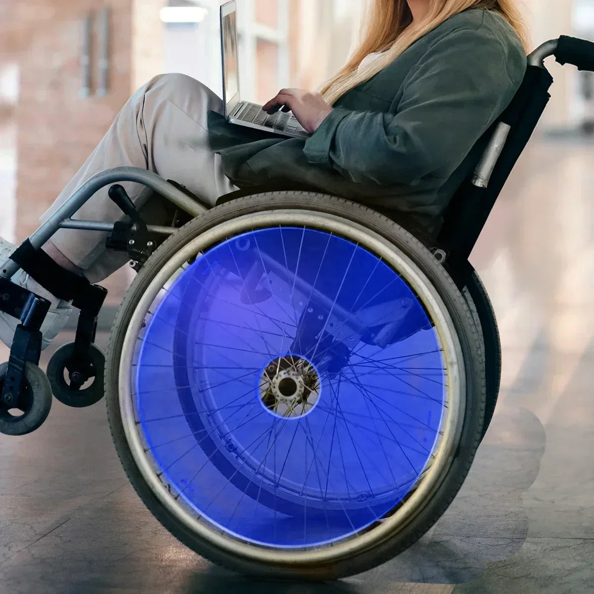 Woman using laptop in wheelchair with blue spoke guards, showcasing durable wheelchair accessories for everyday mobility.