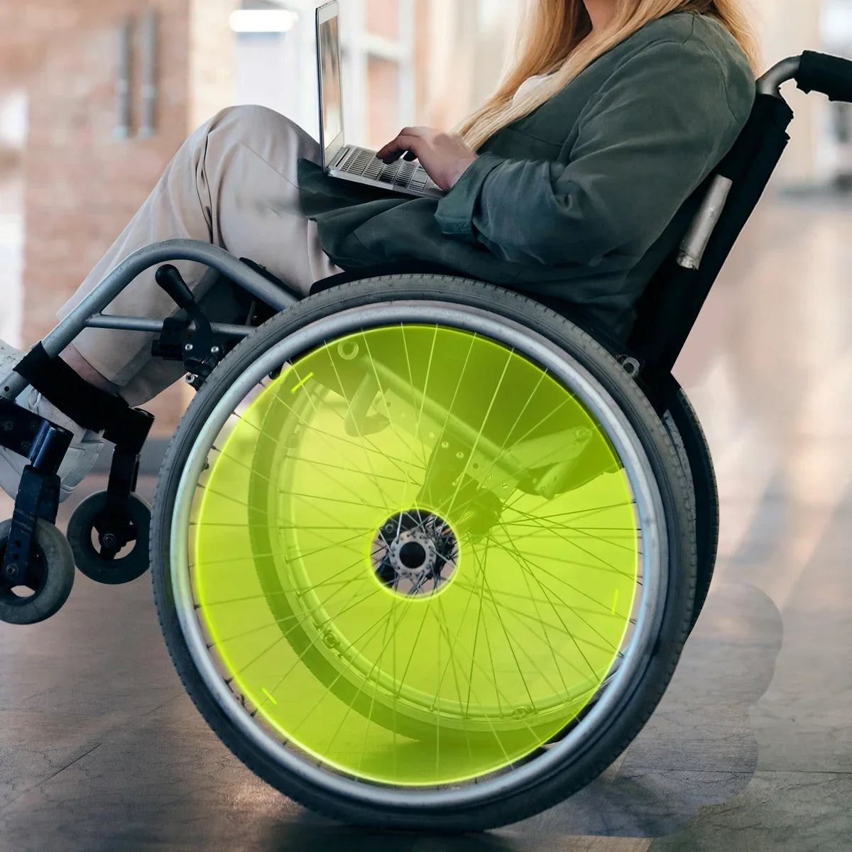 Woman using wheelchair with bright green neon spoke guards, working on laptop indoors