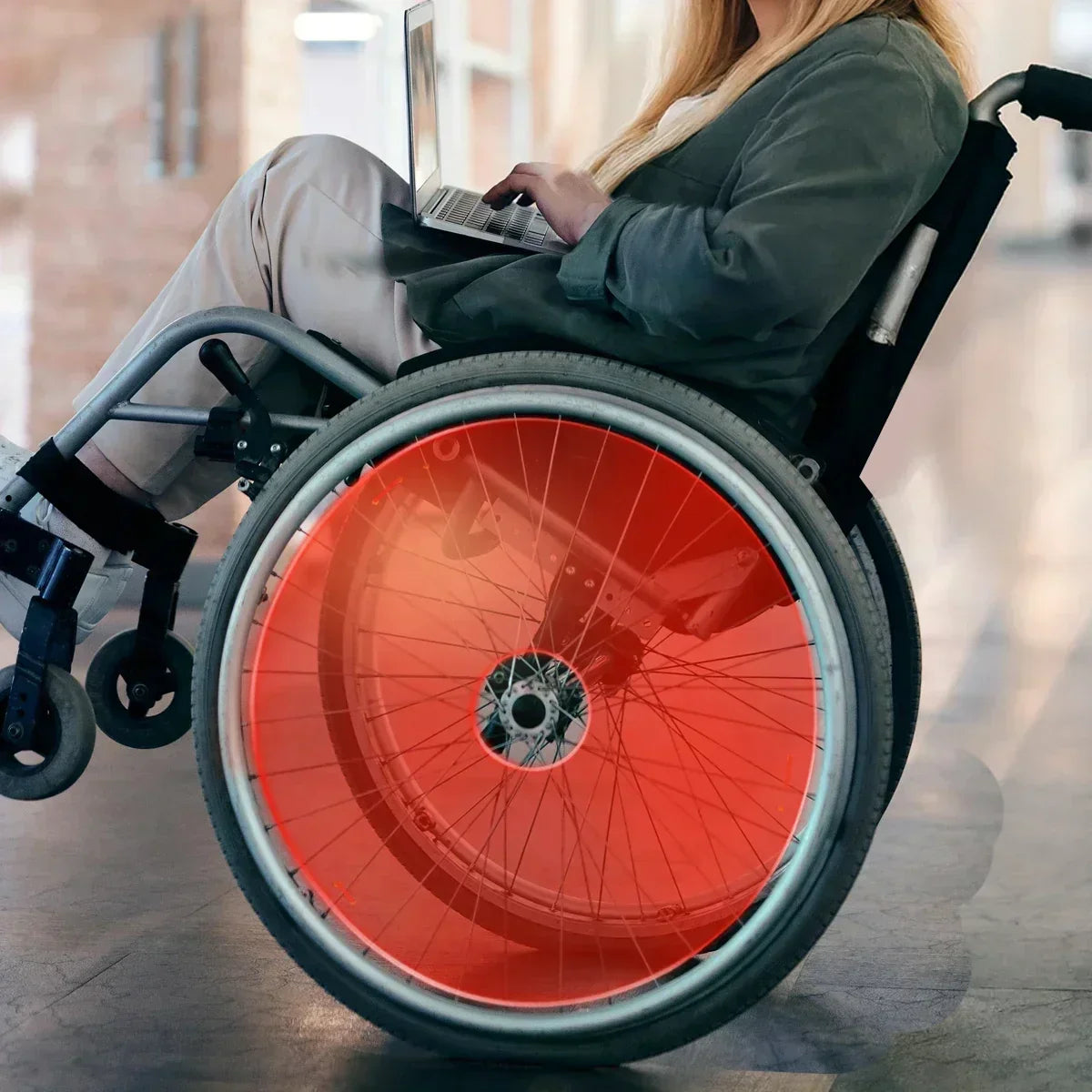 Woman using laptop in wheelchair with red spoke guards, showcasing durable wheelchair accessories for everyday mobility.