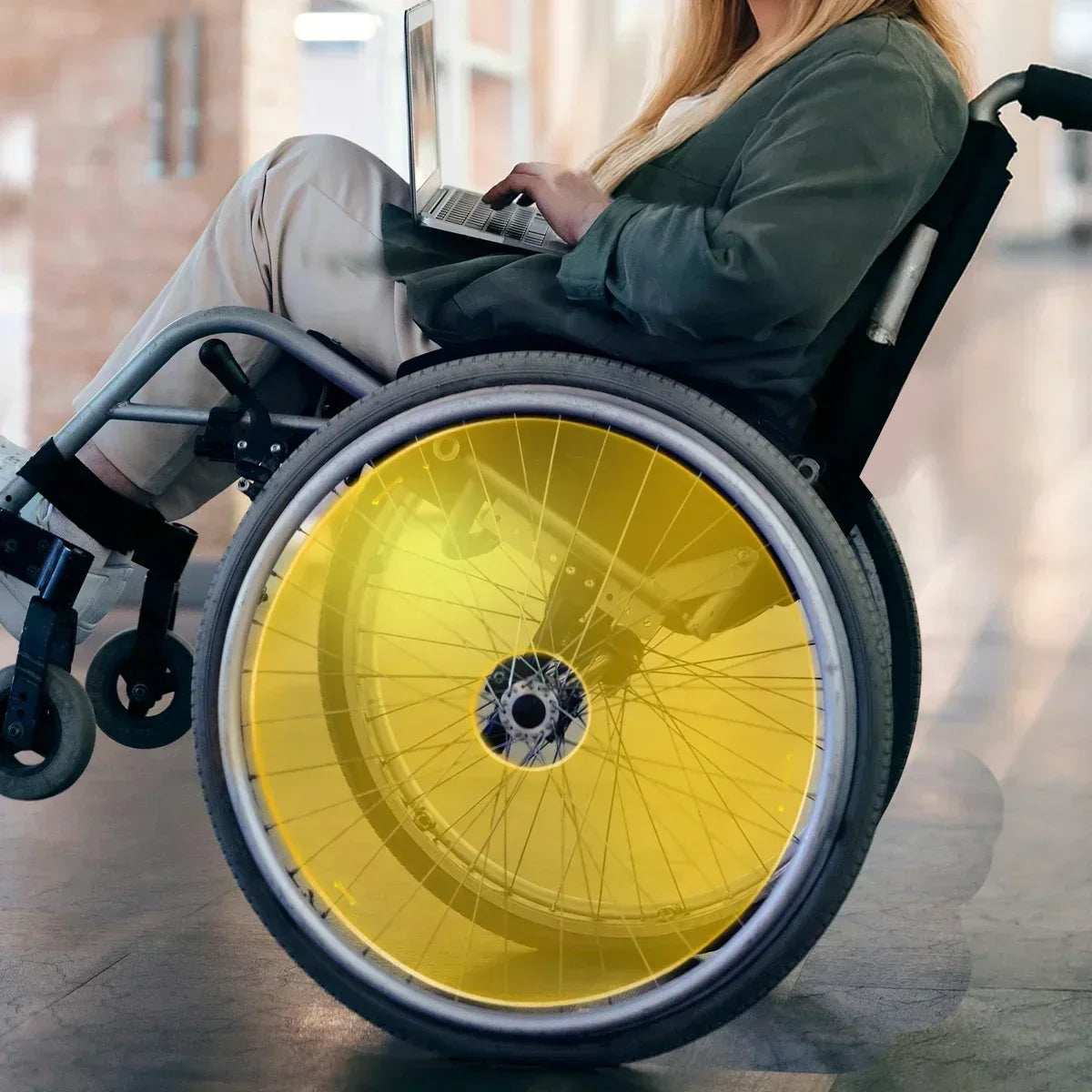Woman using laptop in wheelchair with bright yellow spoke guards, showcasing durable wheelchair accessories for everyday mobility.