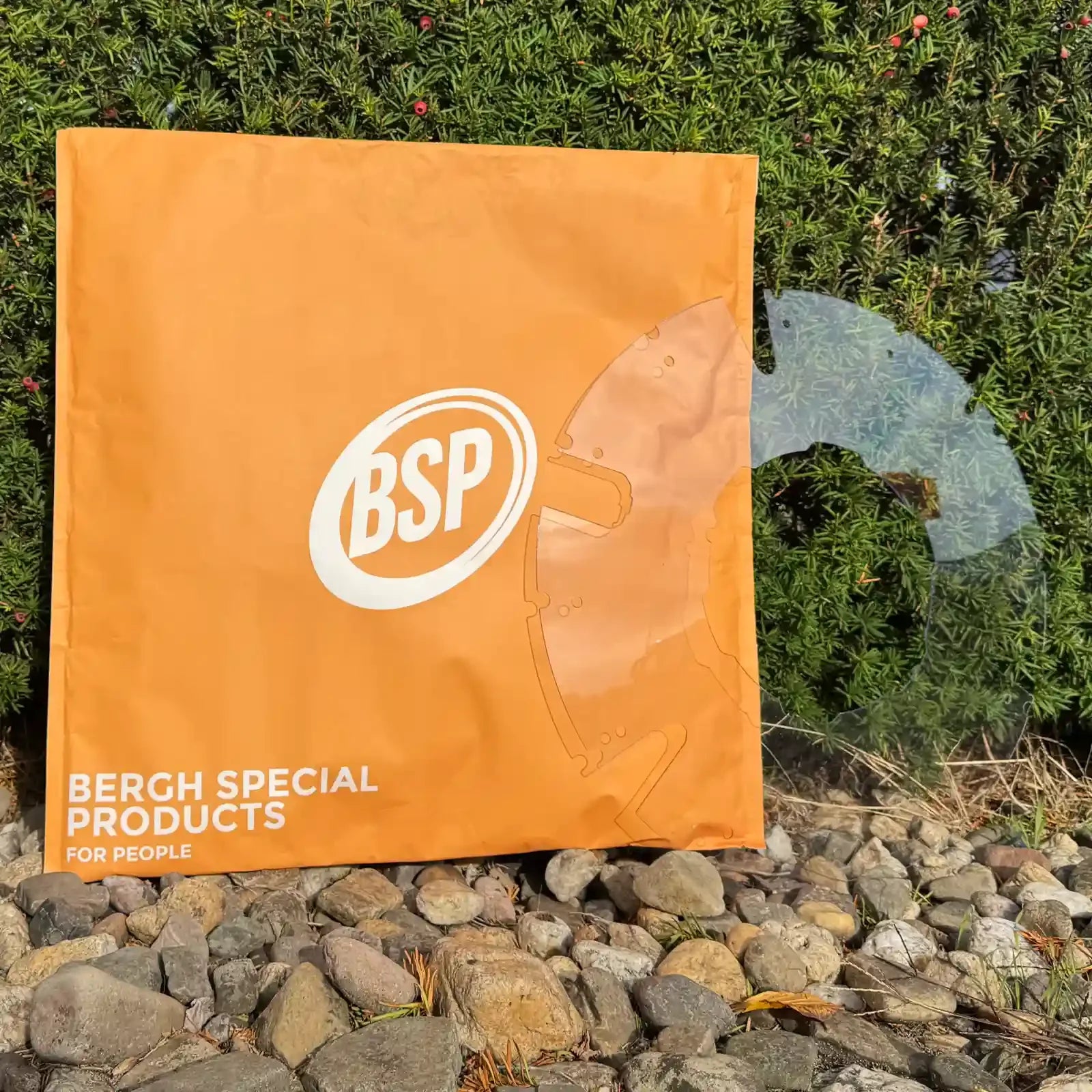 Transparent wheelchair spoke guard displayed outdoors near green hedge and orange bag