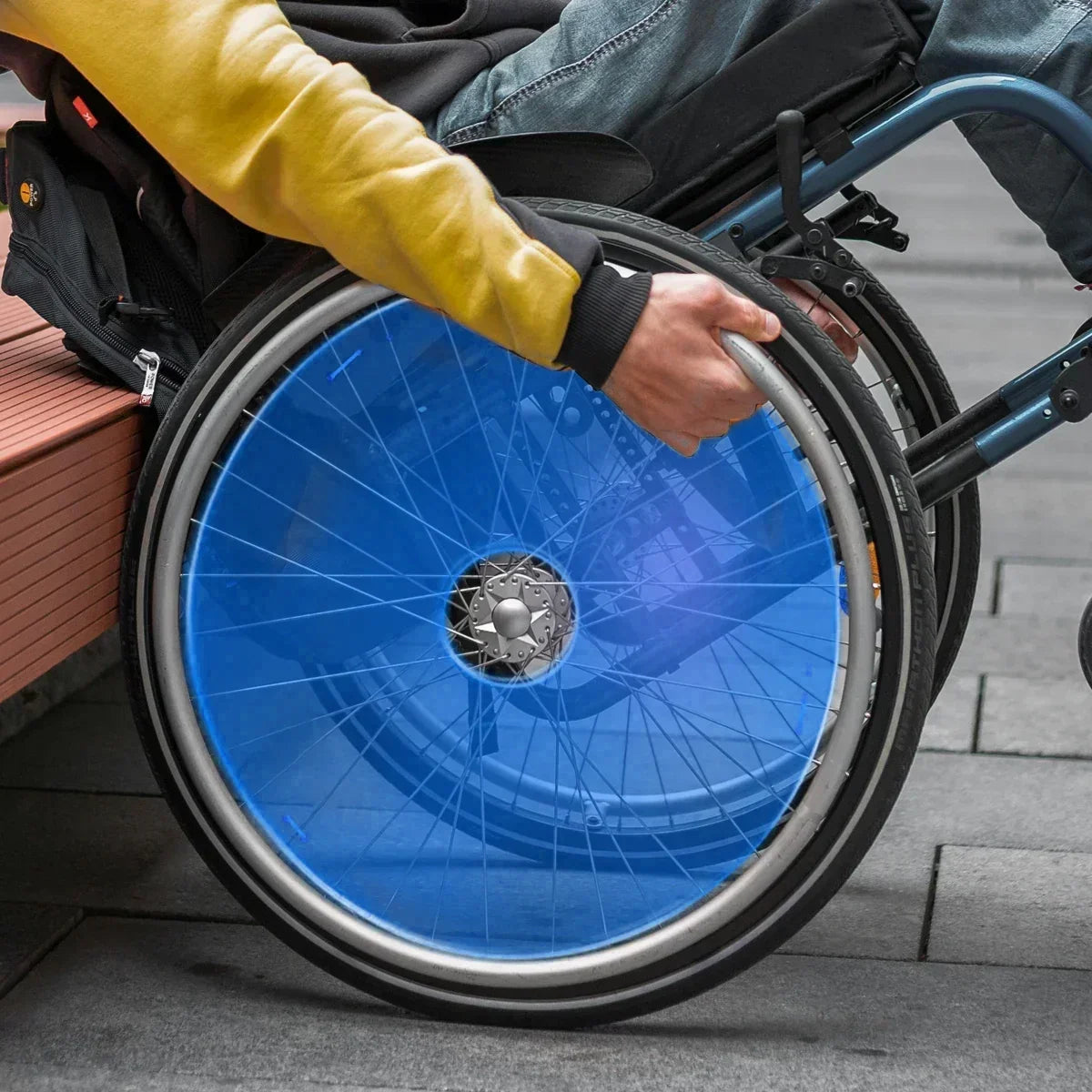 Blue wheelchair spoke guard on manual wheelchair wheel, person gripping rim for mobility
