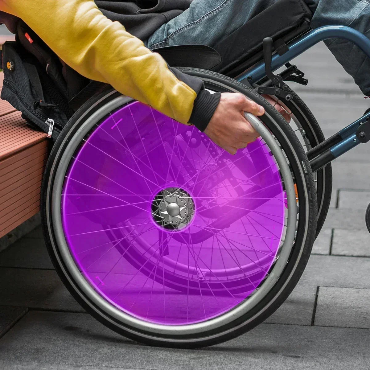 Purple wheelchair spoke guard on manual wheelchair wheel, user gripping rim for mobility