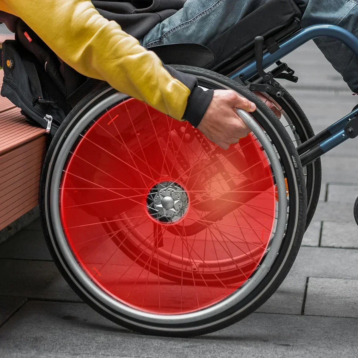 Red wheelchair spoke guard on manual wheelchair wheel, protecting spokes during use
