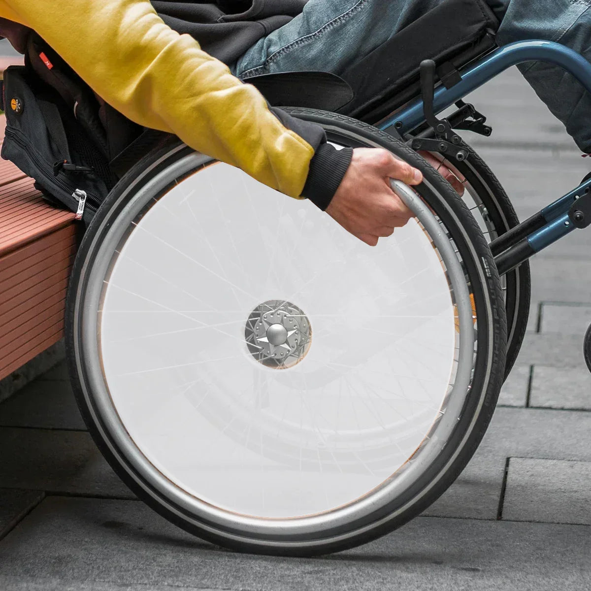 White wheelchair spoke guard on manual wheelchair wheel, person gripping rim outdoors