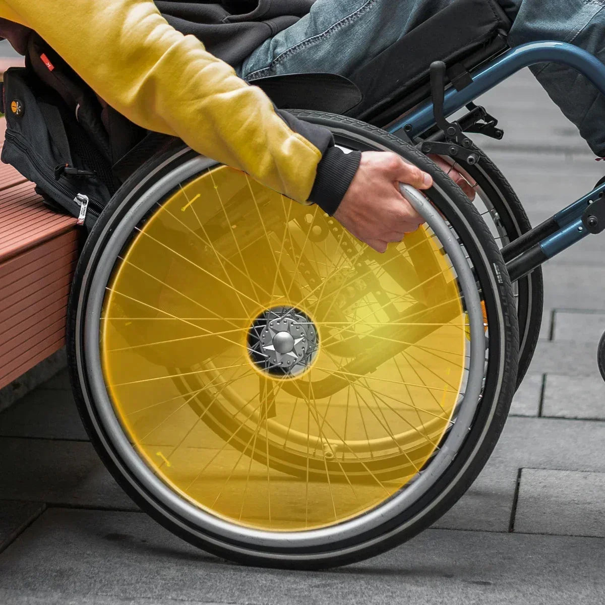 Person gripping wheelchair wheel with bright yellow spoke guard for safety and style