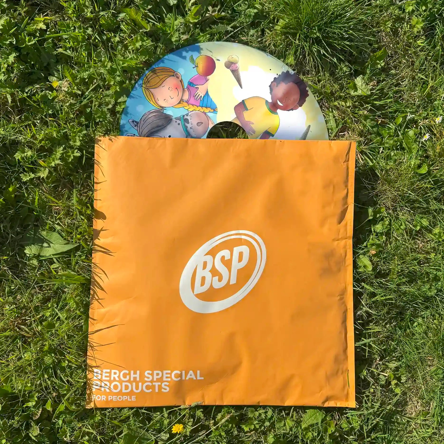 Colorful wheelchair spoke guard with children and pony illustration, partially in orange BSP bag on grass