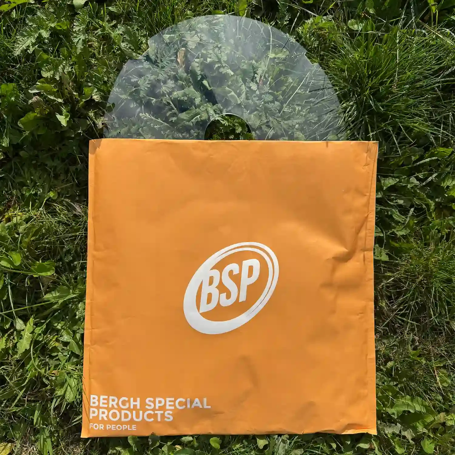 Transparent wheelchair spoke guard with flat cutouts displayed on grass, packaged in an orange BSP bag