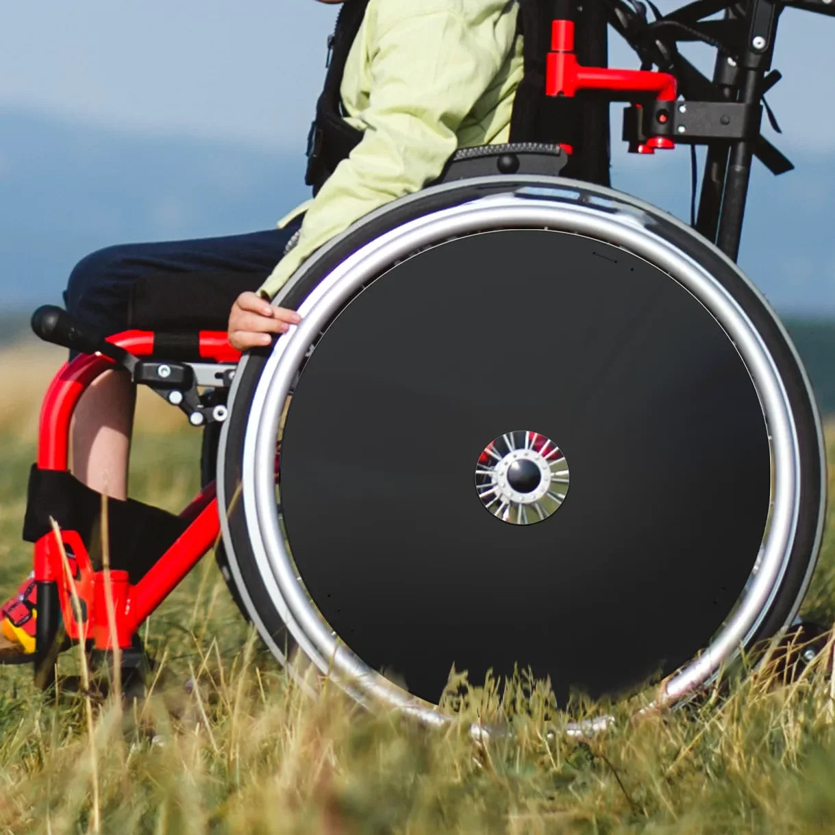 Boy using wheelchair with durable black spoke guards outdoors on grassy field