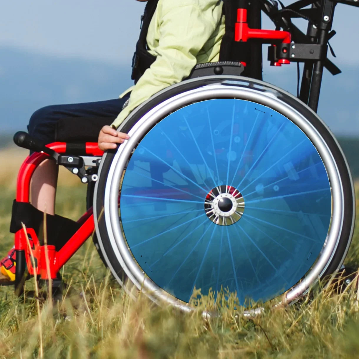 Junge im Rollstuhl mit leuchtend blauem Speichenschutz am Rad draußen auf Gras