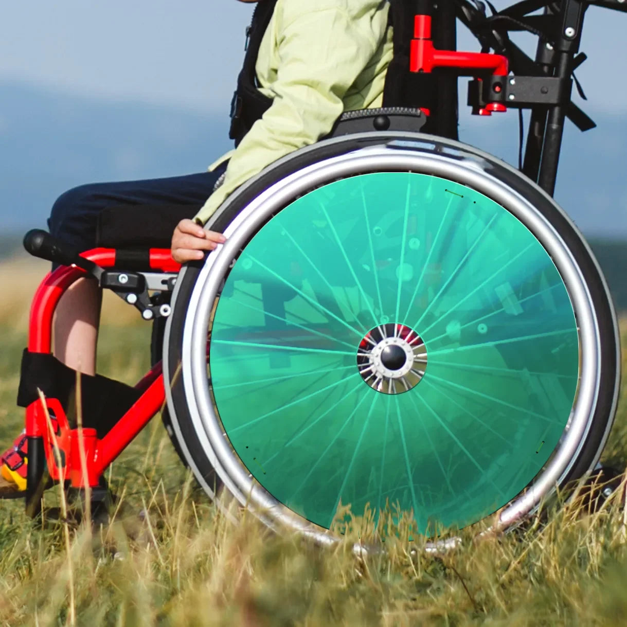 Boy outdoors in red wheelchair with green spoke guards on grassy field