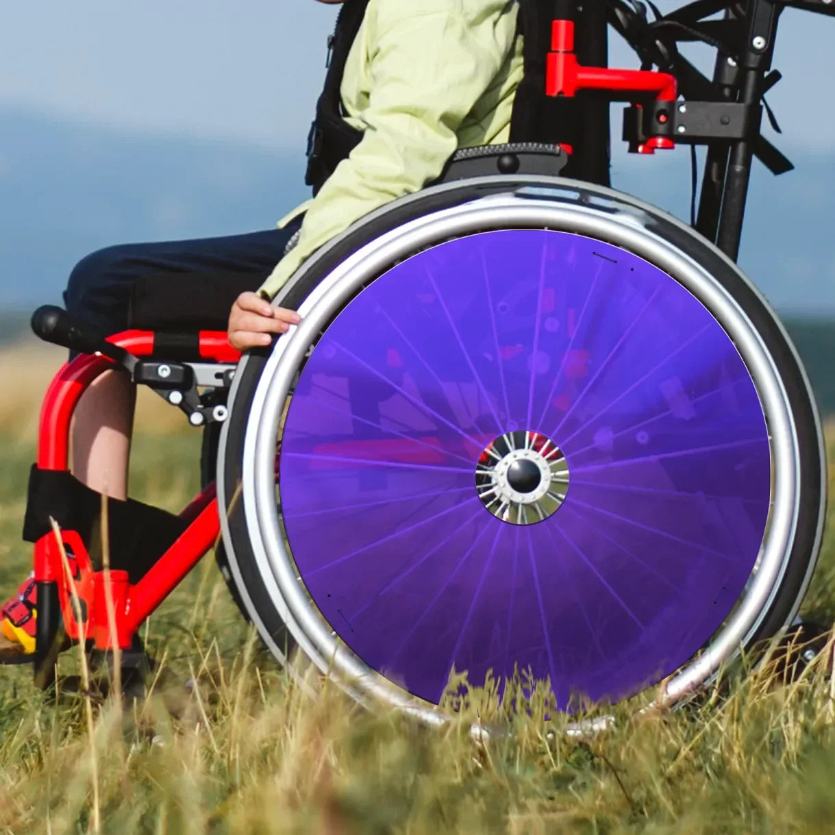 Child in wheelchair with bright purple spoke guards on grass outdoors