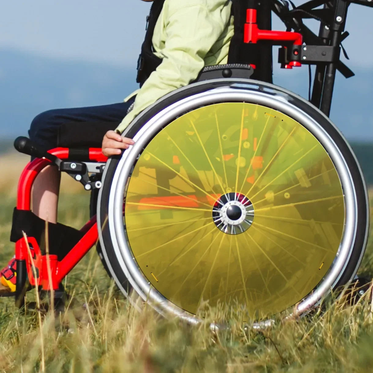 Child in lightweight wheelchair with yellow spoke guards outdoors on grass