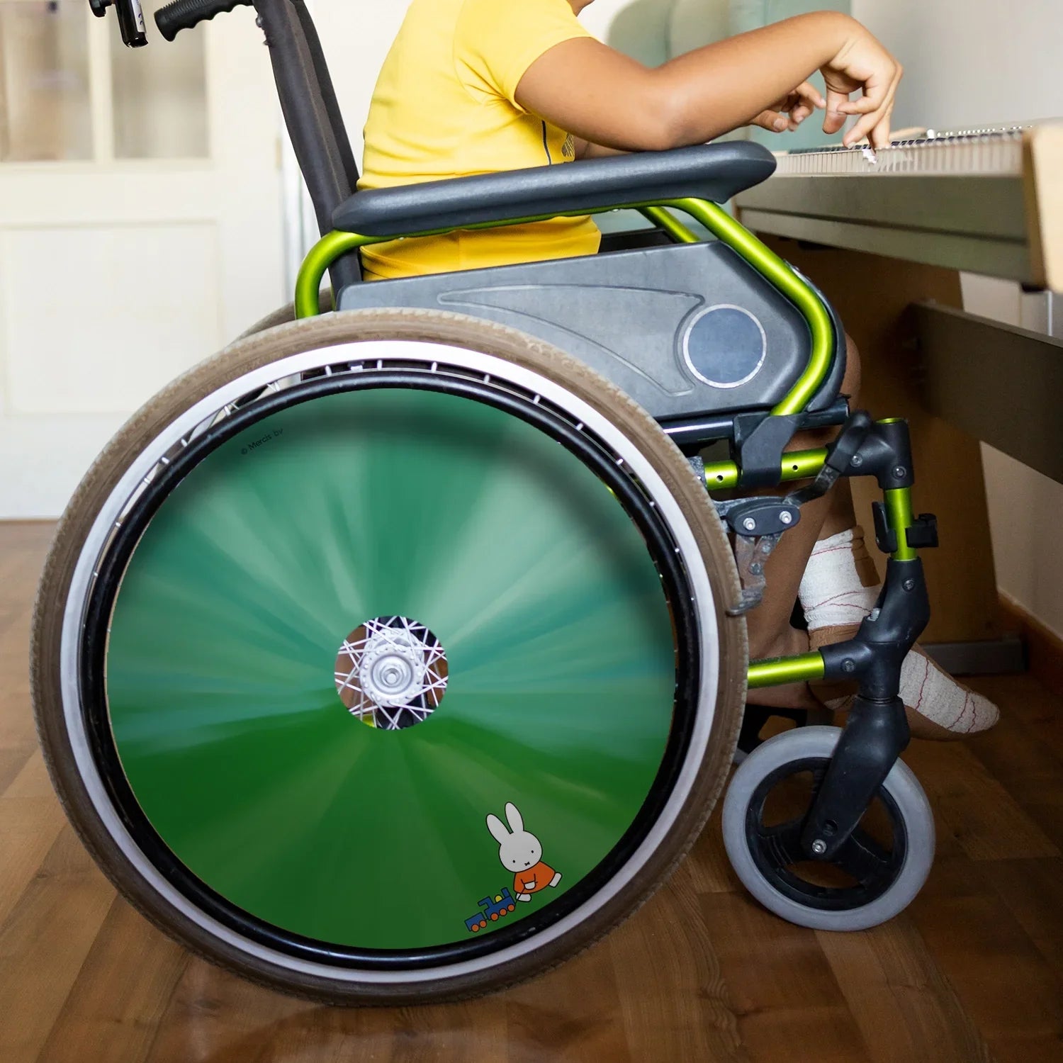 Child in wheelchair with green spoke guard featuring Miffy and toy train design