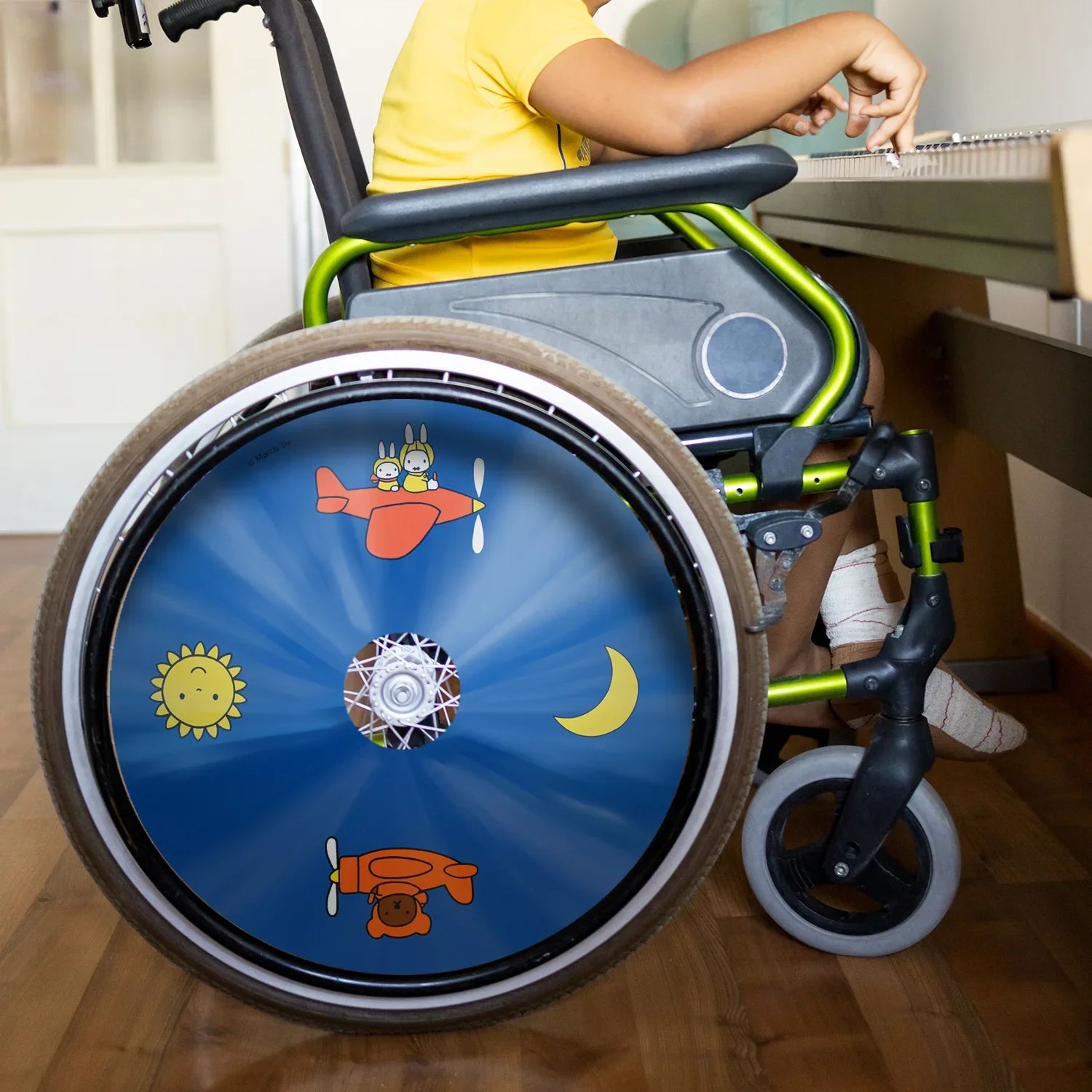 Child in wheelchair with colorful Miffy Air Adventure spoke guard, sun and moon design.
