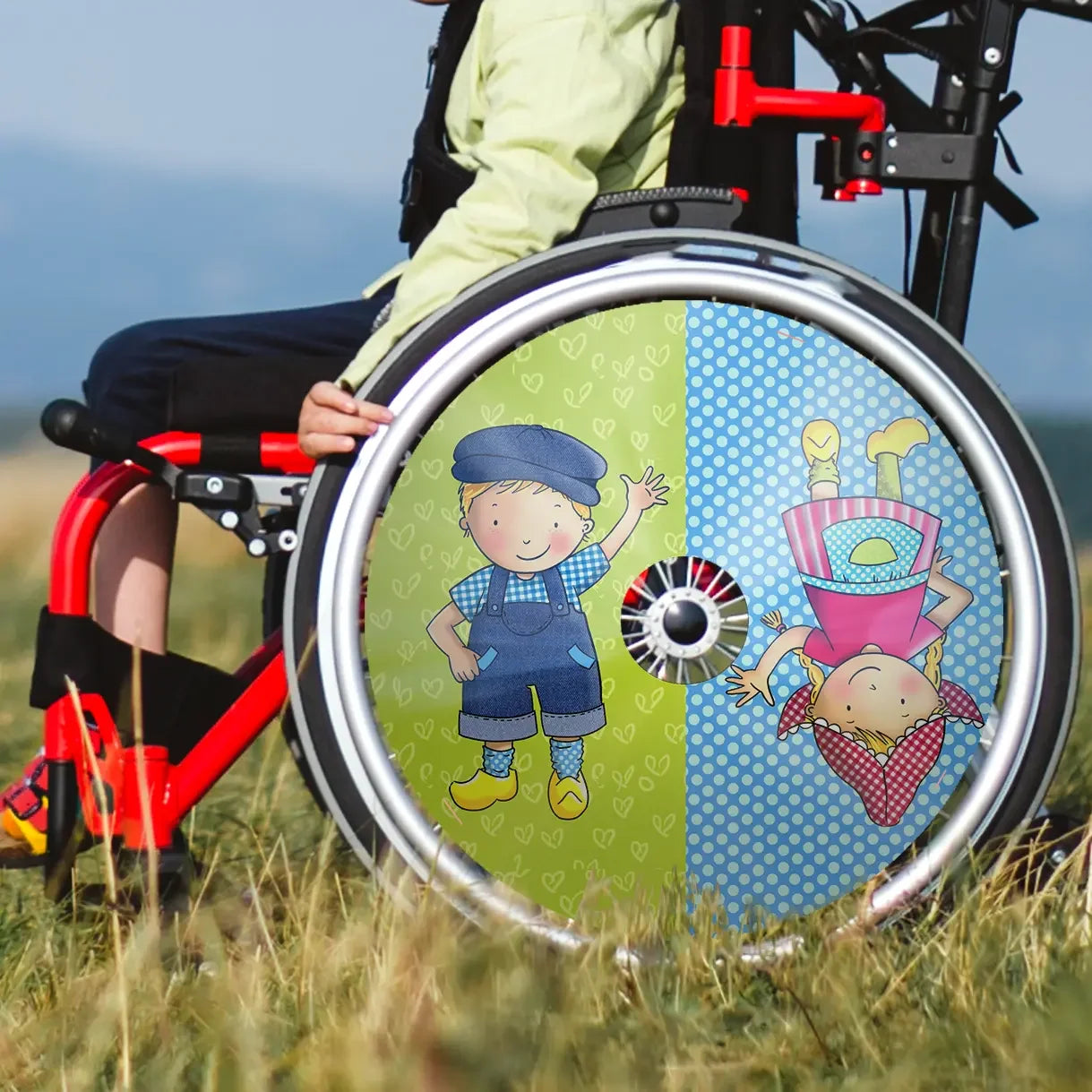 Child in wheelchair with colorful spoke guard featuring cartoon boy and girl design outdoors