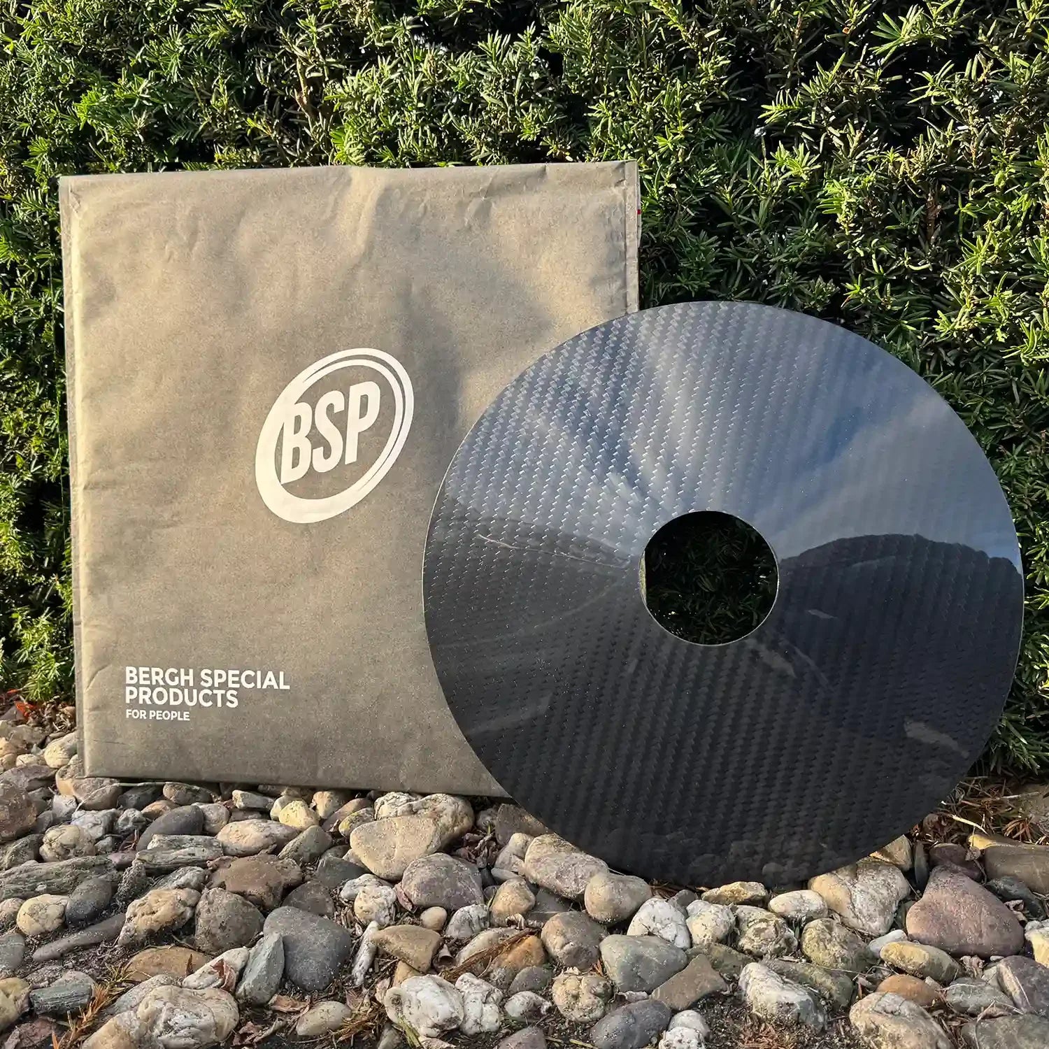 Carbon wheelchair spoke guard and branded pouch on rocks near green hedge