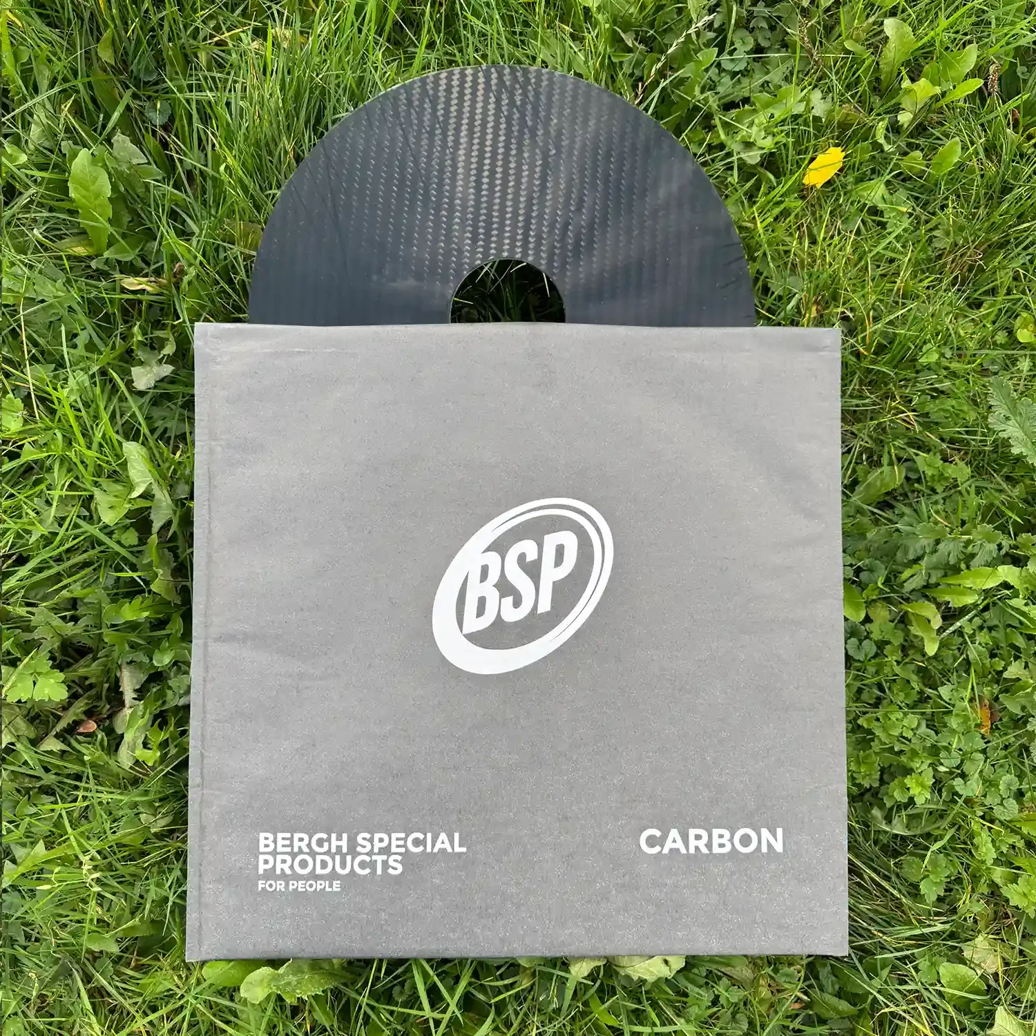 Carbon fiber wheelchair spoke guard partially in grey BSP packaging on green grass