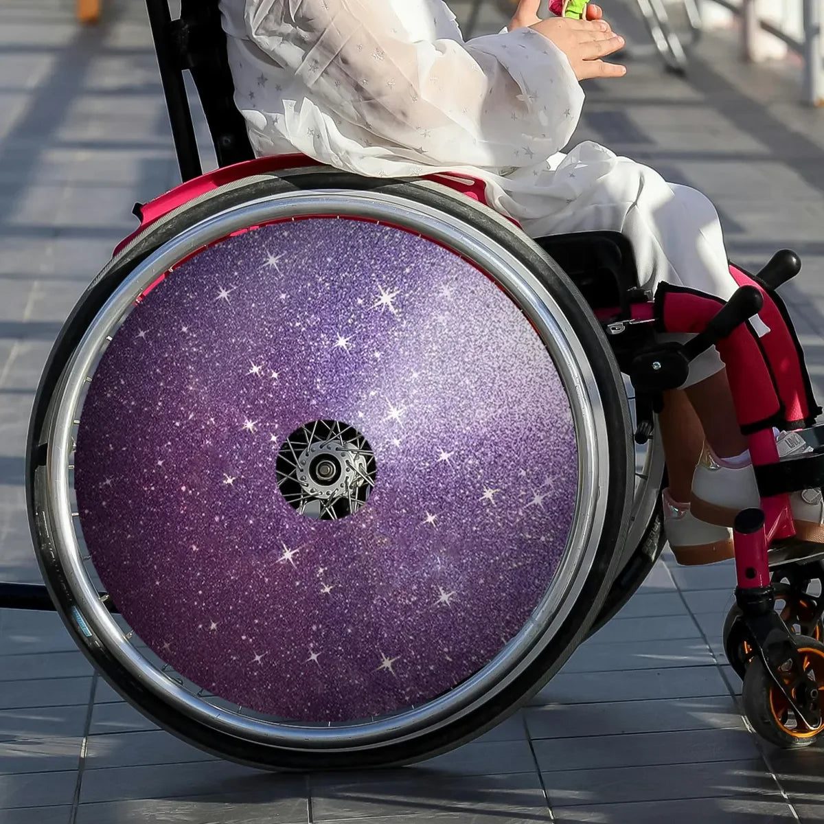 Kind im Rollstuhl mit violettem Sternen-Speichenschutz im Freien