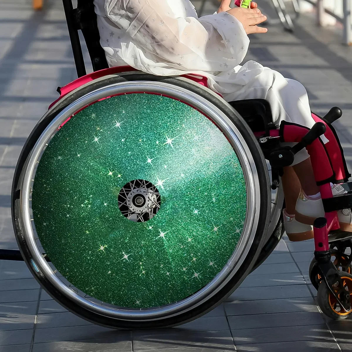 Child in wheelchair with green glitter spoke guards, wheelchair accessories for everyday use