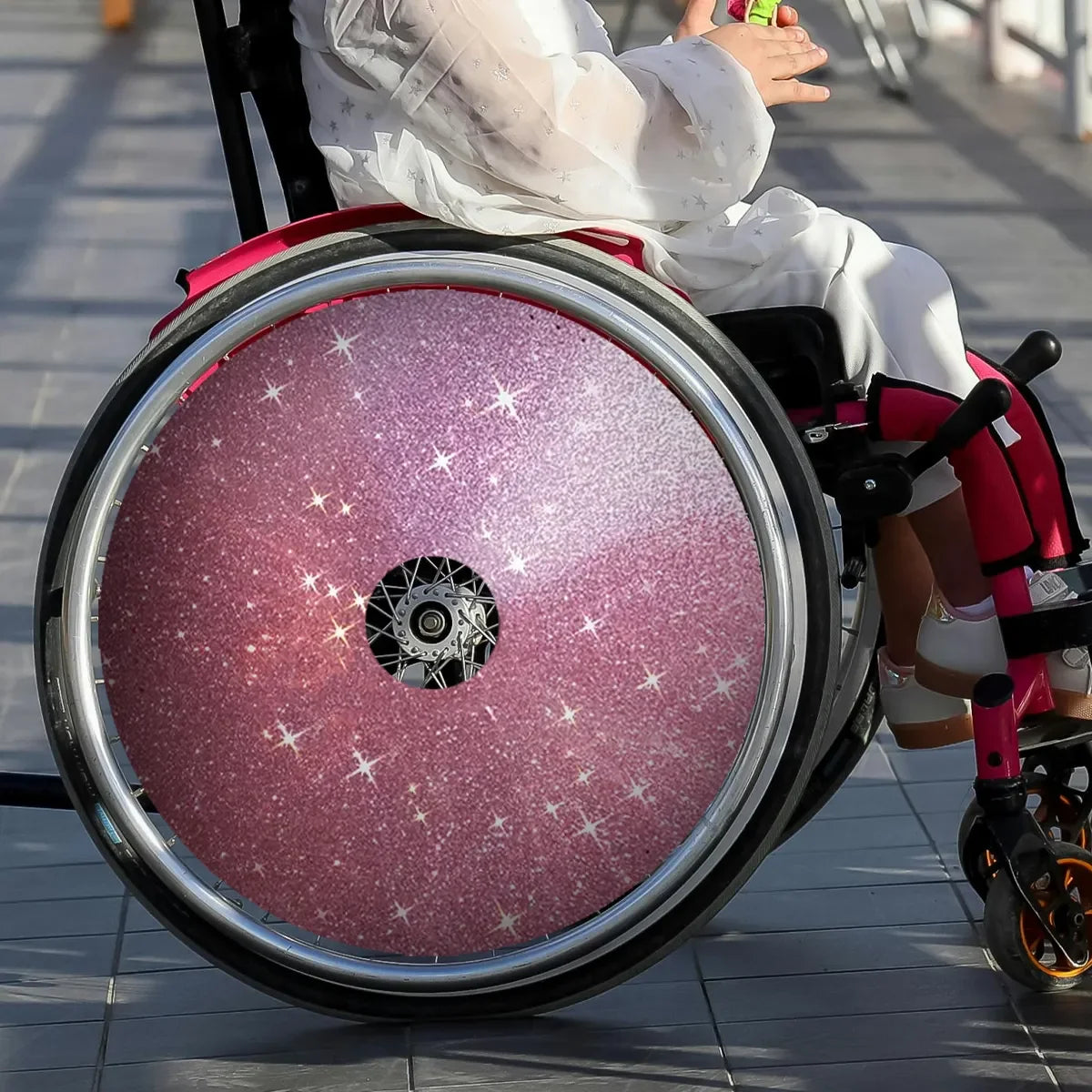 Child in wheelchair with pink glitter star spoke guards, custom wheelchair accessory for kids