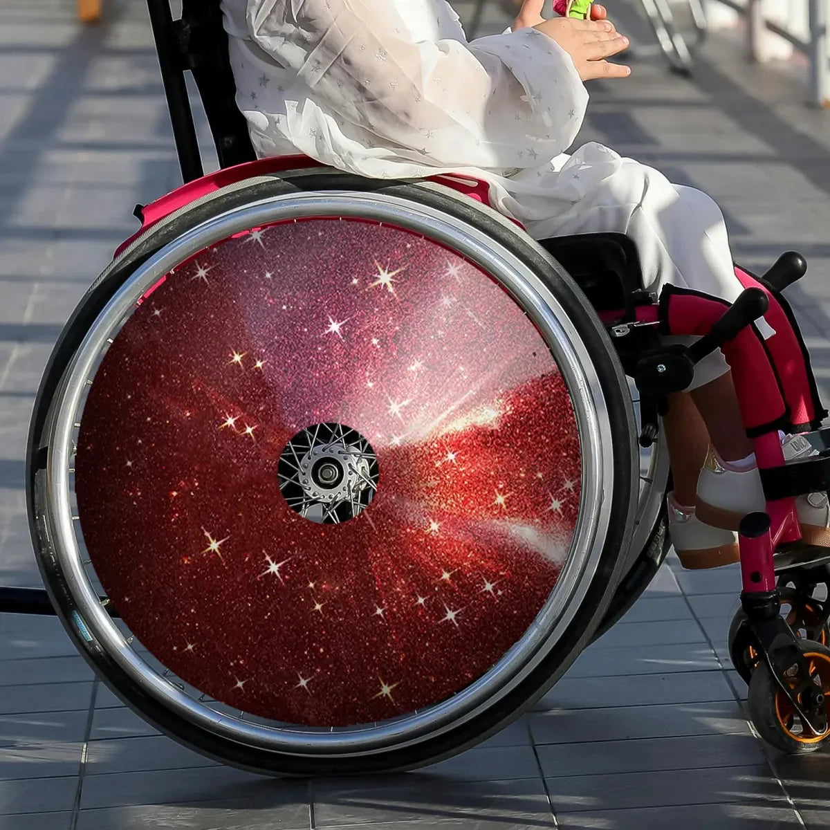 Child in wheelchair with red glitter star spoke guards, custom wheelchair accessory for kids