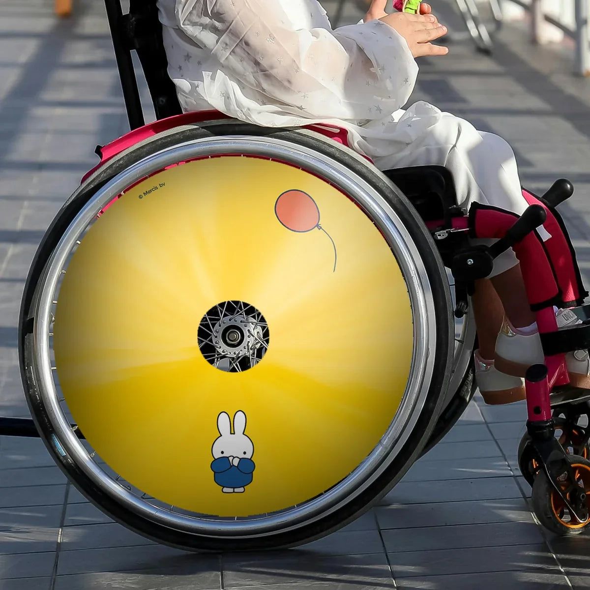 Child in wheelchair with yellow spoke guard featuring Miffy cartoon and red balloon illustration