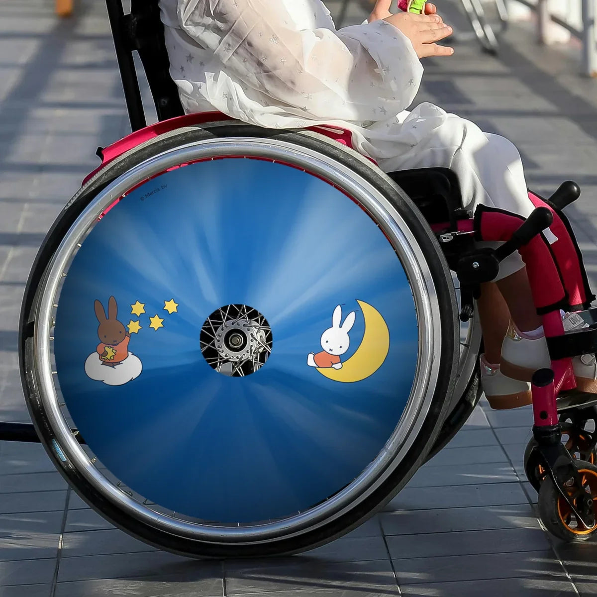 Child in wheelchair with colorful Miffy-themed spoke guards showing stars and moon design