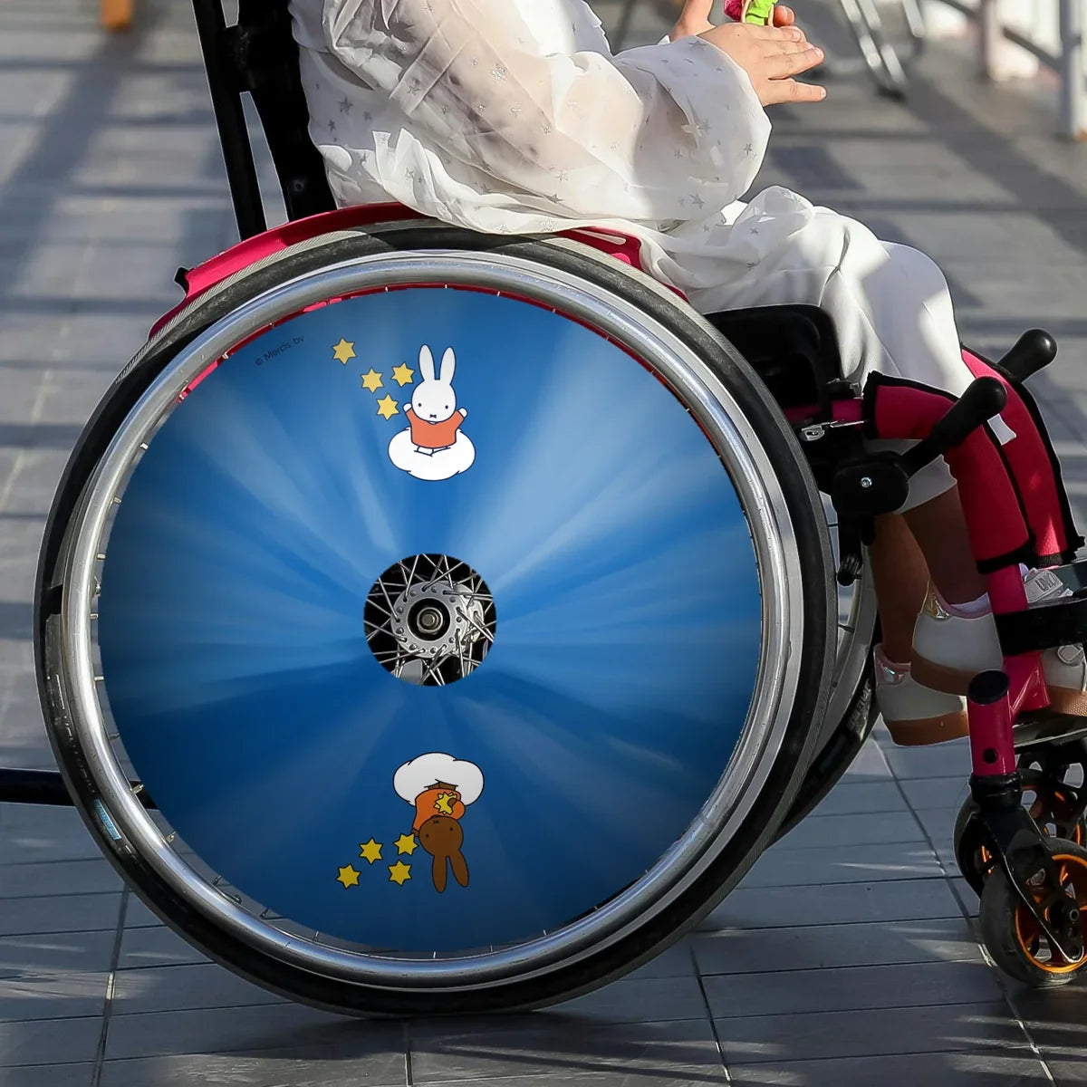 Child in wheelchair with blue spoke guard featuring cartoon bunnies and yellow stars