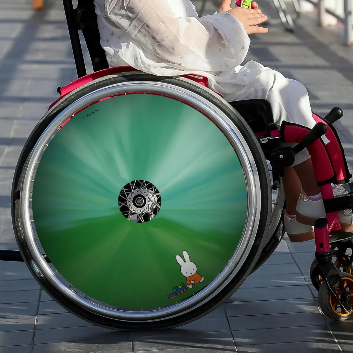 Child in wheelchair with green spoke guard featuring Miffy and toy train design