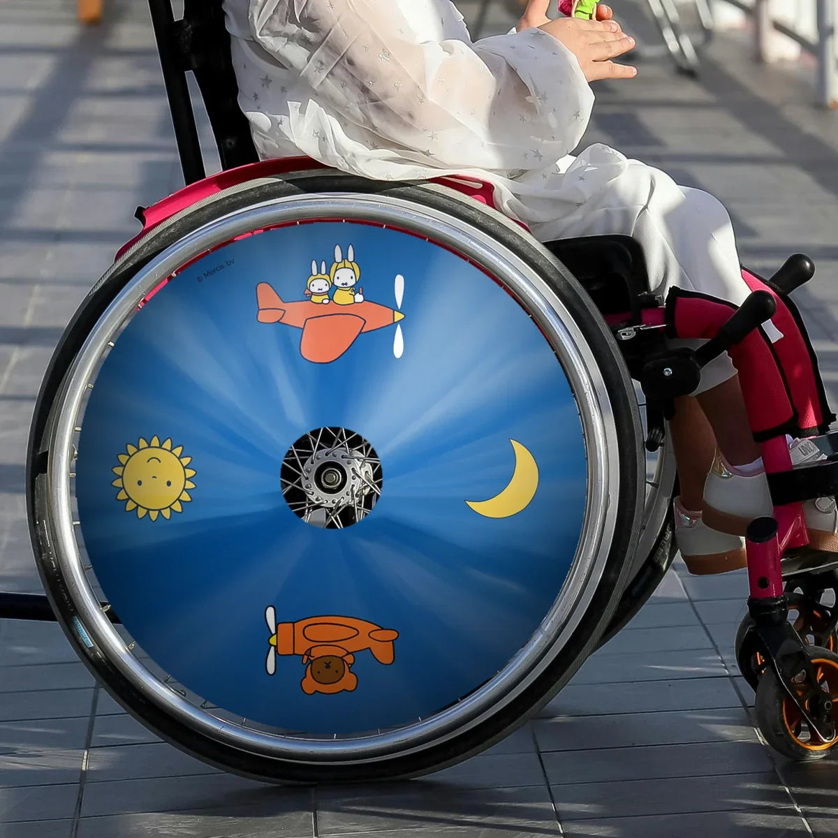 Girl in wheelchair with colorful Miffy Air Adventure spoke guard featuring airplane and sun designs