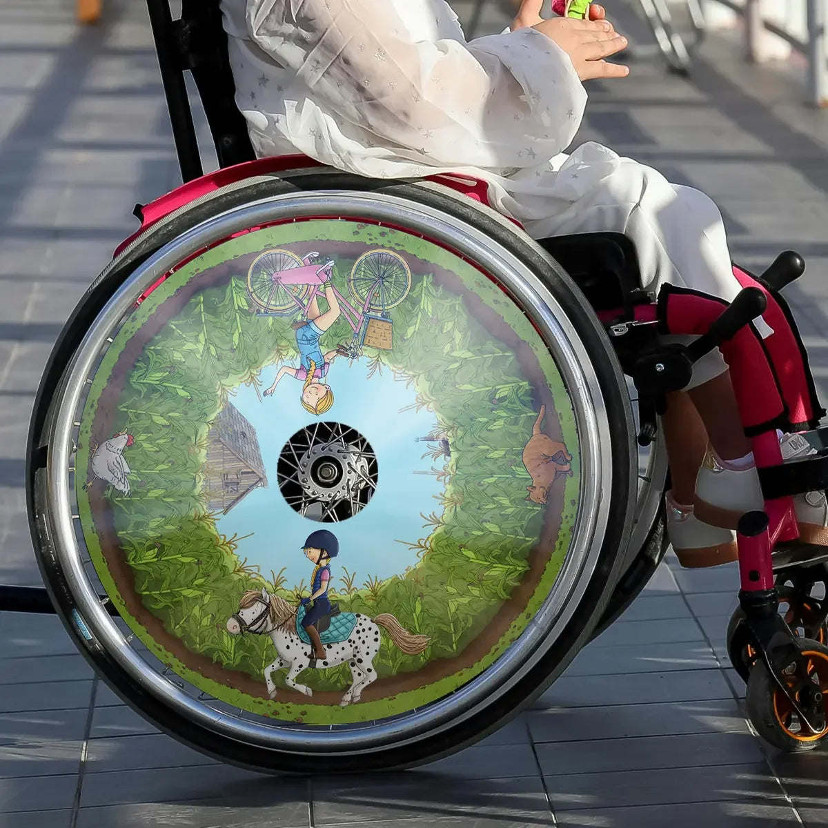Girl in a wheelchair with colorful spoke guard featuring horse and farm cartoon design