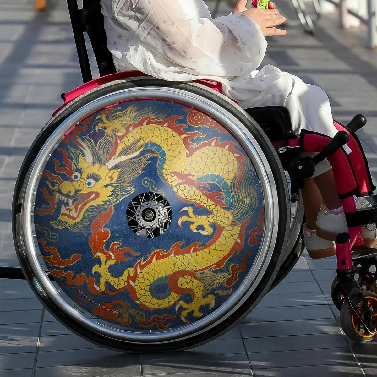 Girl in wheelchair with decorative dragon spoke guards on wheel