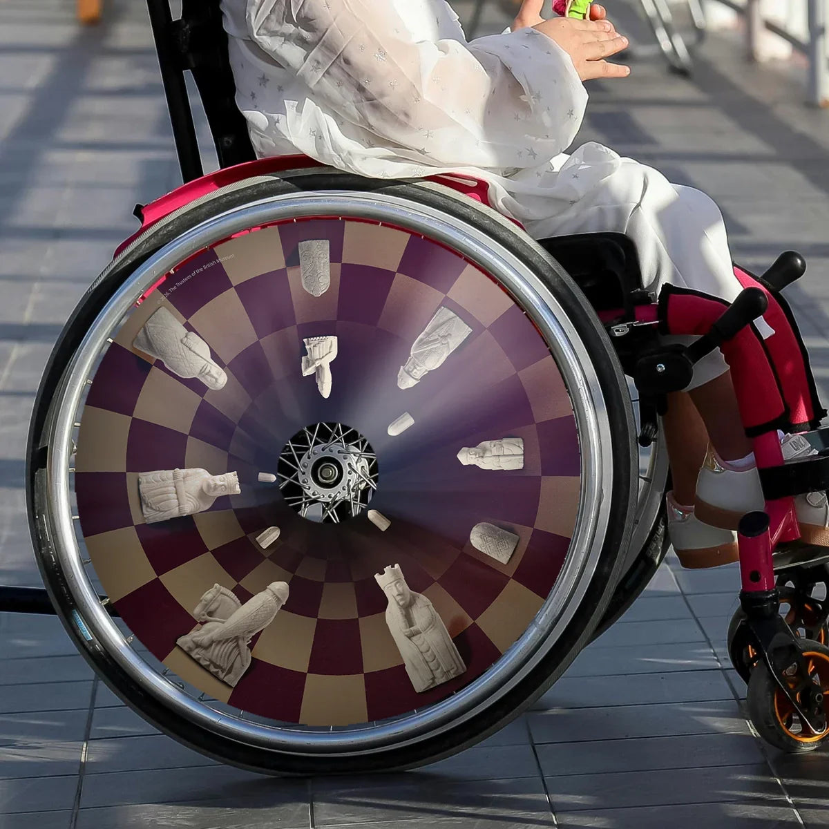 Girl in wheelchair with chess-themed spoke guard featuring Lewis chessmen design