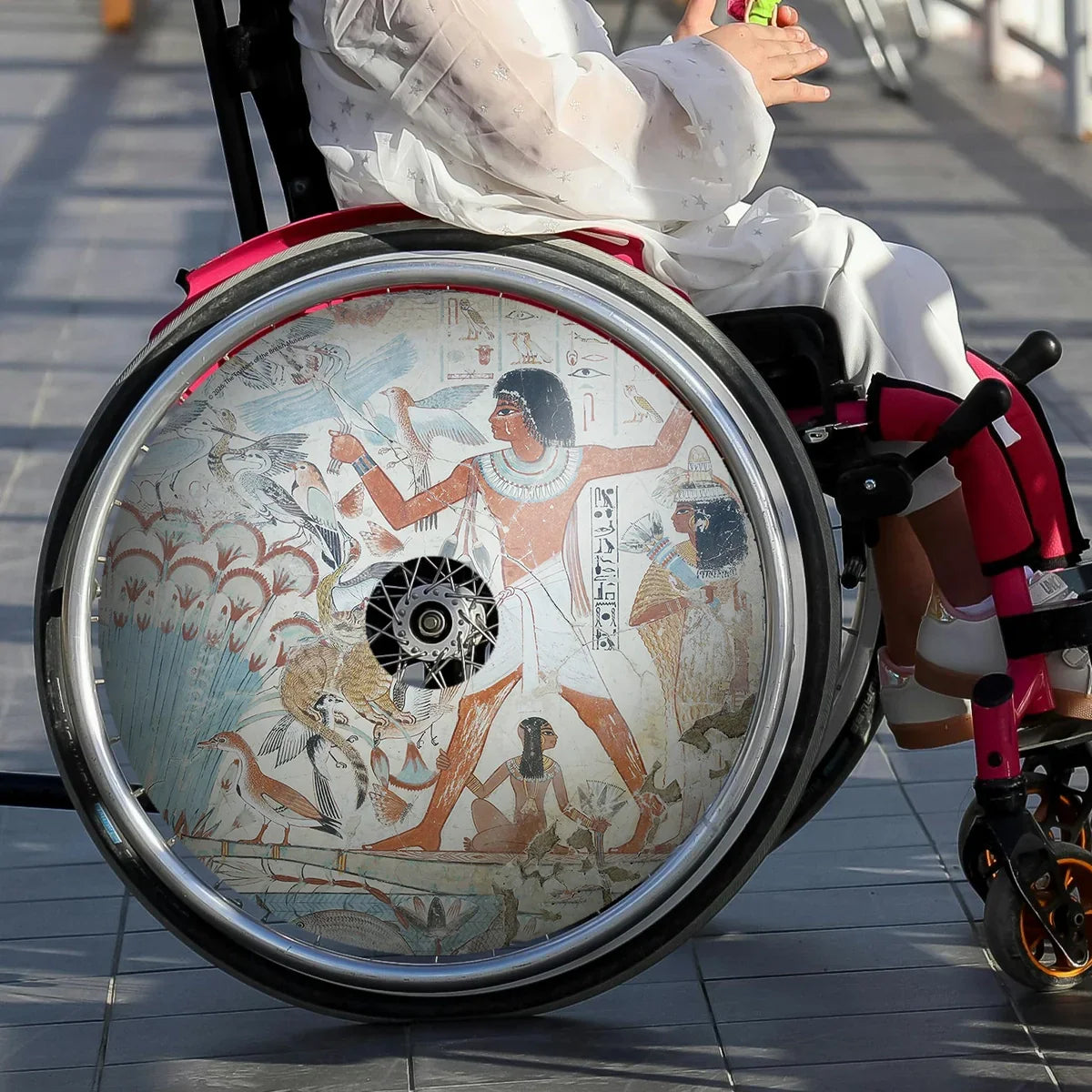 Girl in wheelchair with Egyptian art spoke guard on wheel, wheelchair accessories product