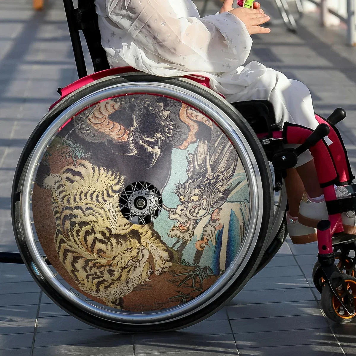 Wheelchair with colorful tiger and dragon spoke guard design, young girl seated outdoors