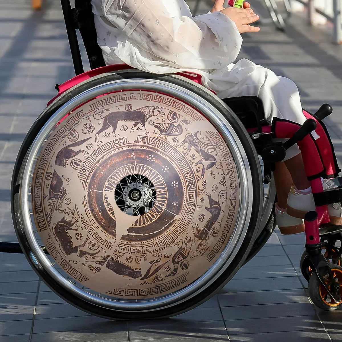 Girl in wheelchair with decorative wild goat spoke guard on wheel, orthopedic supports visible