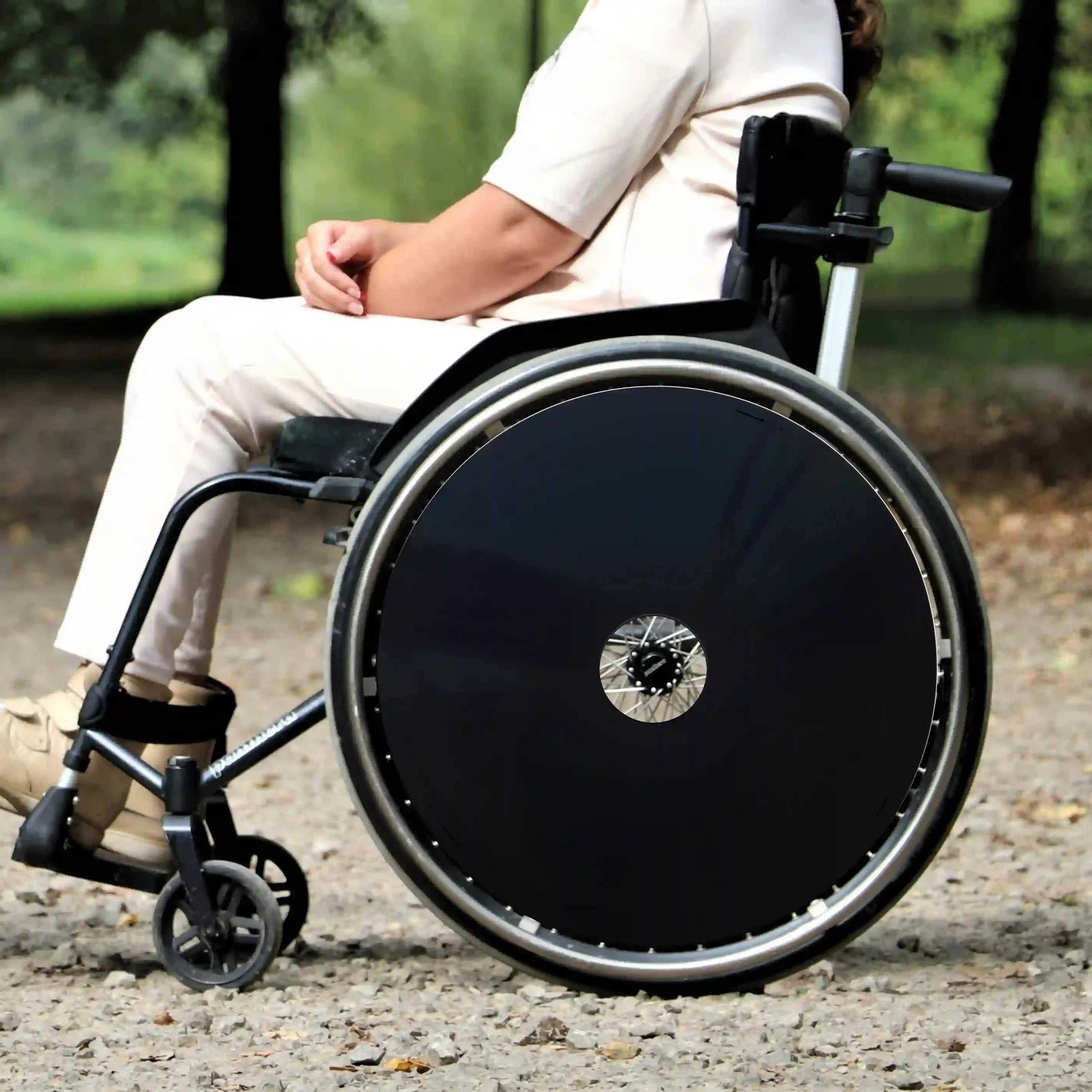 Woman sitting in wheelchair outdoors with black spoke guards on wheels