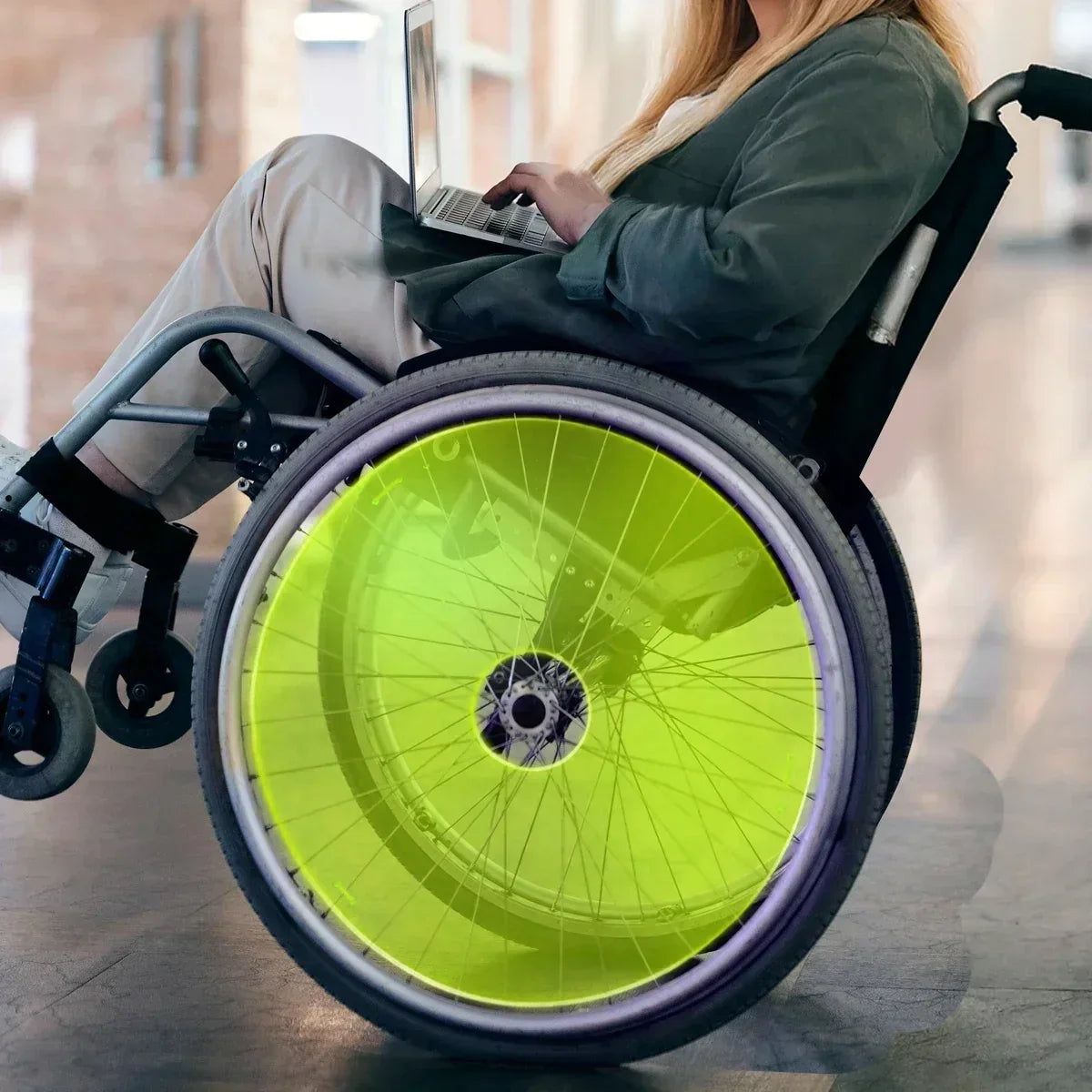Bright lime green wheelchair spoke guard on manual wheelchair wheel, woman using laptop